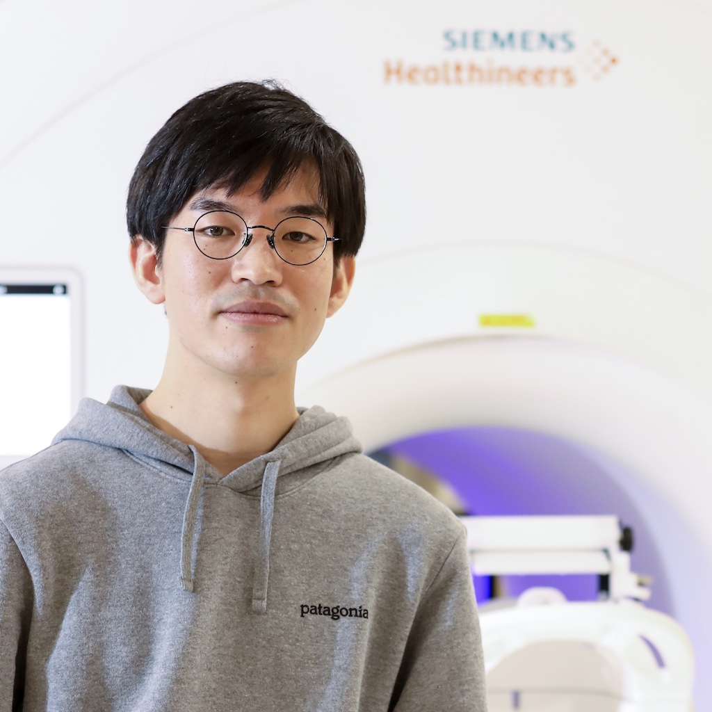 Portrait of Teruaki Kido, standing in front of an MRI scanner
